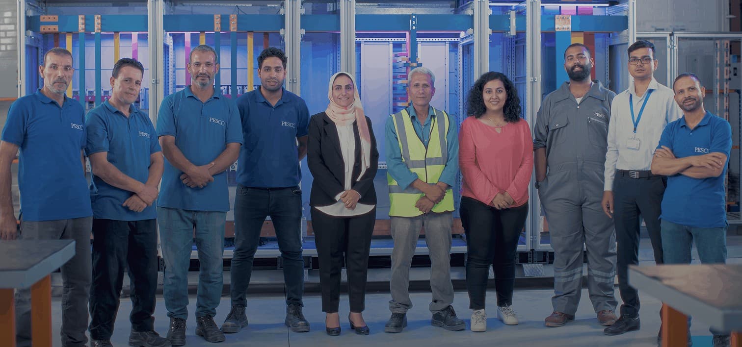 The PESCO team standing together in front of switchgear panels in the fabrication facility